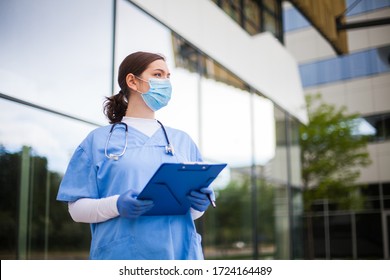 Young Female Caucasian UK Doctor Looking In Distance With Fear Worry Anxiety  Uncertainty In Eyes,wearing Uniform  Face Mask,hope  Faith  Overcoming Global Coronavirus COVID-19 Pandemic Crisis