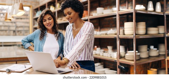 Young female ceramists using a laptop while working together. Two female entrepreneurs managing online orders in their store. Happy young businesswomen running a successful small business together. - Shutterstock ID 2209881015