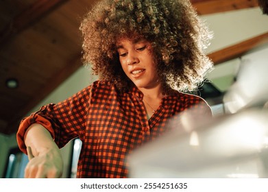 Young female chef with curly hair is focused on preparing a dish in a professional kitchen, possibly in a restaurant or other culinary setting - Powered by Shutterstock