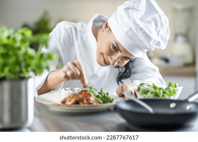 A young female chef finishes the meal with herbs in the restaurant kitchen. - Powered by Shutterstock