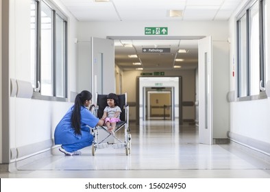 Young Female Child Patient In Wheelchair Sitting In Hospital Corridor With Indian Asian Female Nurse