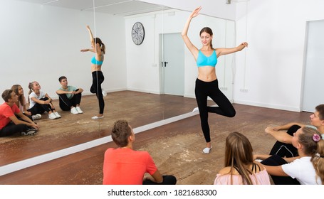 Young female coach holding group dance training with teenagers in modern dance hall..