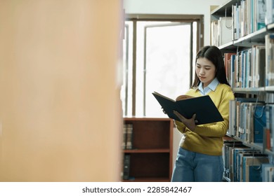 Young female college highschool student in casual outfit standing, reading or choosing books to read at library for studying, academic research, school work, project, or exam. - Shutterstock ID 2285842467