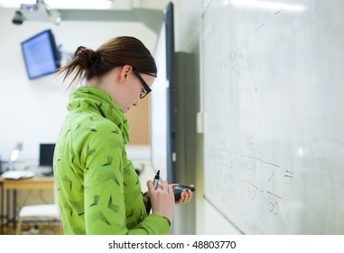 Young Female College Student In Front Of A Whiteboard Using A Calculator During Math Class