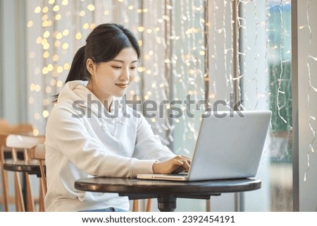 Young female college student model sitting at a table in an indoor cafe in South Korea, Asia, looking at a laptop, listening to a lecture, doing homework, or working	
