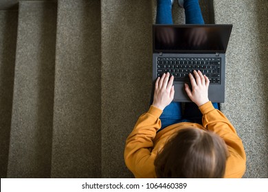 Young Female College Student Sitting On Stairs At School, Writing Essay On Her Laptop. Education Concept. View From Above.