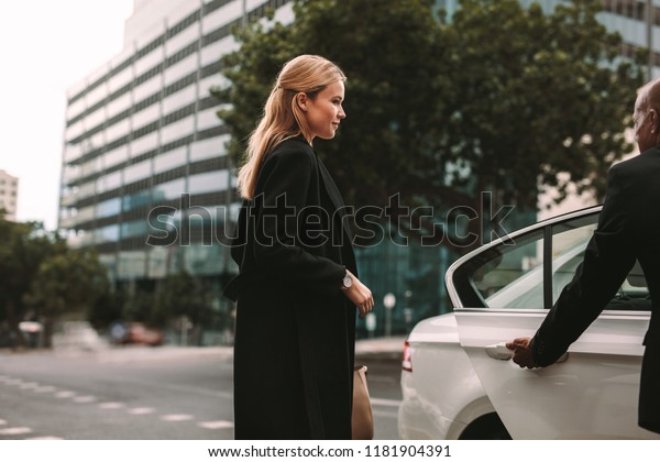 Young female commuter getting\
into a taxi. Businesswoman entering a taxi with driver opening\
door.