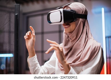 Young female company worker having briefing with modern technology. Muslim business woman in VR glasses standing at office room and gesturing with hands. Concept of people and augmented reality. - Powered by Shutterstock