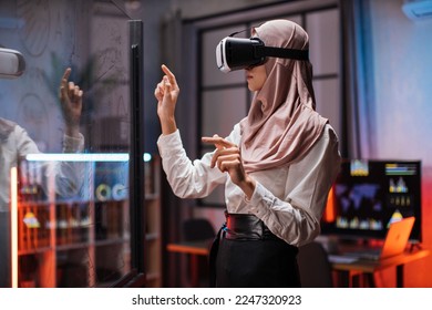 Young female company workers wearing VR headset while having meeting at office room. Confident muslim woman in hijab using innovative technology during business strategy. - Powered by Shutterstock