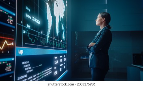 Young Female Computer Science Engineer Looking At Big Screen Display Showing Global Map With Data Points. Telecommunications Technology Company System Control And Monitoring Room With Servers.