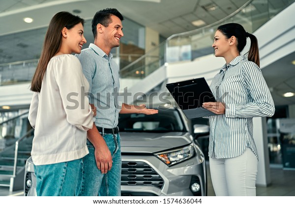 Young female\
consultant and couple buyers signing contract for new car in auto\
show. Concept for car\
rental.