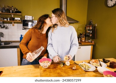 Young female couple kissing while preparing breakfast in their home kitchen. Lesbian couple savoring tea and exchanging kisses in the cozy atmosphere of their kitch - Powered by Shutterstock