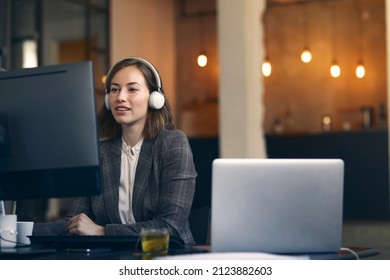 Young female creative editor working on the computer while wearing headphones. Her office looking very mordern and cool. Concept: busy businesswoman at work.