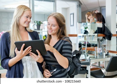 Young female customer holding digital tablet while standing with hairdresser at parlor - Powered by Shutterstock