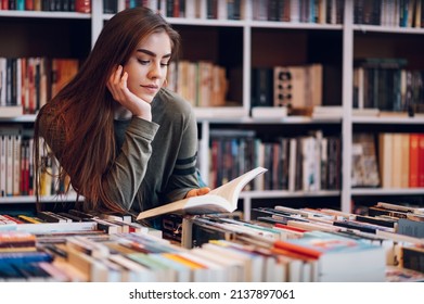 Young female customer reading a book in bookstore while buying some good literature. Woman picking a book to read.