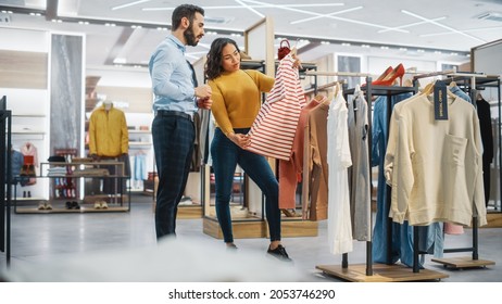 Young Female Customer Shopping In Clothing Store, Retail Sales Associate Helps With Advice. Diverse People In Fashionable Shop, Choosing Stylish Clothes, Colorful Brand With Sustainable Designs