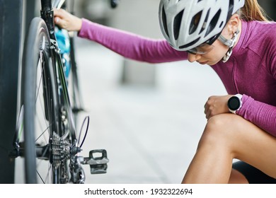 Young female cyclist in protective gear looking focused while checking her bicycle, standing outdoors on a daytime - Powered by Shutterstock