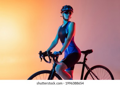 Young Female Cyclist Riding A Bicycle Isolated On Studio Background In Gradient Yellow Pink Neon Light. Concept Of Active Life, Rest, Travel, Energy, Sport. Fit Caucasian Woman As Model