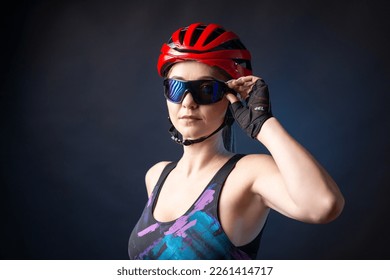 A young female cyclist wearing a safety helmet and glasses, dressed in a bib shorts poses against a black background in the studio. - Powered by Shutterstock