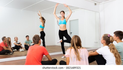 Young female dance teacher giving dance class for teens, showing ballet movements ..