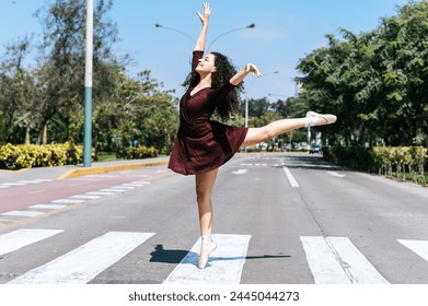 Young female dancer showcases ballet pose on an urban crosswalk with trees in the background - Powered by Shutterstock