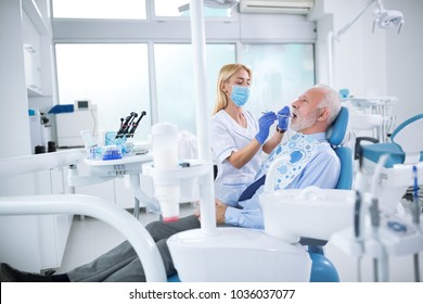 A Young Female Dentist Controls Health Of The Tooth Of An Older Patient