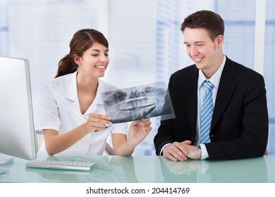 Young female dentist showing jaw Xray to businessman in clinic - Powered by Shutterstock