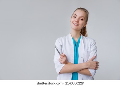 Young Female Dentist Wearing In Uniform With Tweezers And Mirror Isolated On White