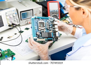 Young Female Digital Electronic Engineer Examining Computer PC Motherboard In Laboratory