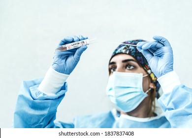 A Young Female Doctor Attempts To Do A Covid Test. She Wears Healthcare PPE. She Inserts The COVID Nasopharyngeal Swab In The Tube. Standard COVID Sample Collection Kit.