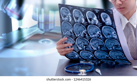 Young Female Doctor Holding MRI Or CT Scan Picture, Doctor In Uniform Sitting In Working Room And Holding X-ray Picture For Diagnosis Brain Injury Or Cerebrovascular Accident Of Patient 