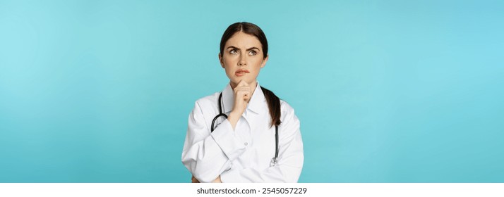 Young female doctor, hospital worker in white coat, thinking and looking away thoughtful, searching solution, standing over toquoise background. - Powered by Shutterstock