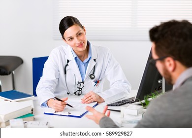 Young female doctor listening intently to a male patient explaining his symptoms or asking a question as they discuss paperwork together in a consultation