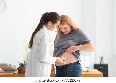 Young Female Doctor Measuring Fat Layer Of Overweight Woman With Caliper In Clinic