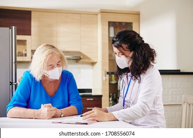 Young Female Doctor In Medical Mask Showing Prescription To Senior Patient