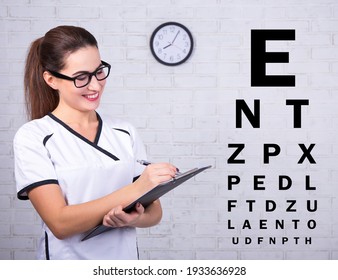 Young Female Doctor Ophthalmologist With Eye Test Chart Over White Brick Wall Background