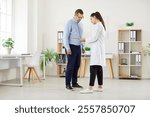 Young female doctor physiotherapist or nurse measure waist with measuring tape for mature man patient standing in medical clinic during examination. Slimming, weight loss and diet concept.