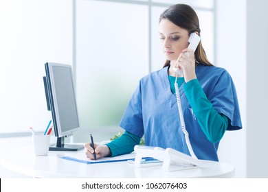 Young female doctor and practitioner working at the reception desk, she is answering phone calls and scheduling appointments