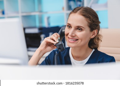 Young female doctor practitioner working at reception desk while answering phone calls and scheduling appointments