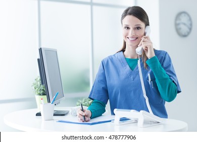 Young female doctor and practitioner working at the reception desk, she is answering phone calls and scheduling appointments