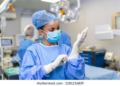 Young female doctor prepares for surgery, wears blue surgical gloves, in a coat and mask - Powered by Shutterstock