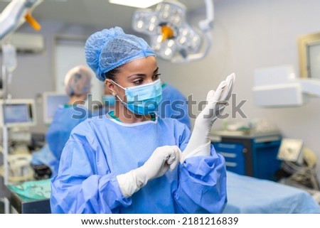 Young female doctor prepares for surgery, wears blue surgical gloves, in a coat and mask Foto stock © 