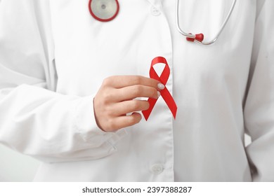 Young female doctor with red ribbon, closeup. World AIDS day concept