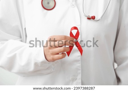 Young female doctor with red ribbon, closeup. World AIDS day concept