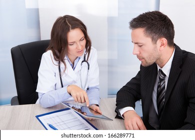 Young Female Doctor Showing Digital Tablet To Businessman - Powered by Shutterstock