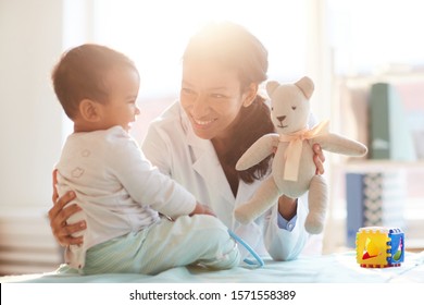 Young female doctor smiling and playing with baby boy during her visit