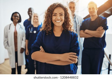 Young female doctor smiling while standing in a hospital corridor with a diverse group of staff in the background