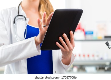 Young Female Doctor Standing In Clinic Reading A File Or Dossier On The Tablet Computer