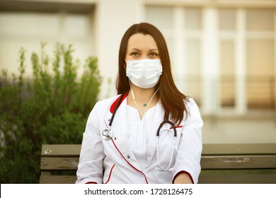 Young Female Doctor In Surgical Mask And Earbuds During Online Webinar Or Conference Outdoors Via Wireless Internet