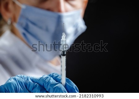 A young female doctor with a syringe looks at the camera. A nurse wearing a medical mask and blue latex gloves. Medicine and health care. Vaccination for the virus. Preventive measures against the